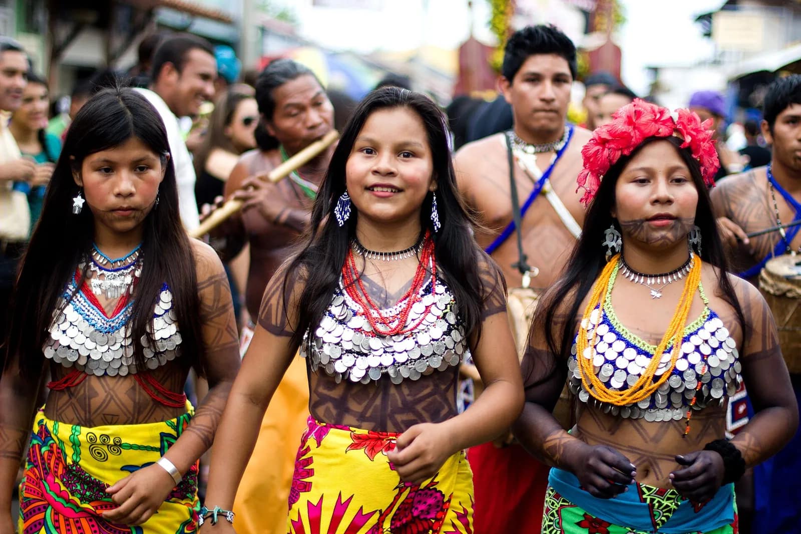 Miembros de la comunidad indígena Emberá en Panamá vistiendo trajes tradicionales, recibiendo visitantes en su aldea a orillas del río en la selva tropical.